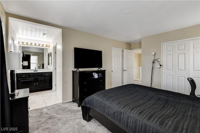 bedroom featuring baseboards, light colored carpet, ensuite bathroom, light tile patterned flooring, and a sink