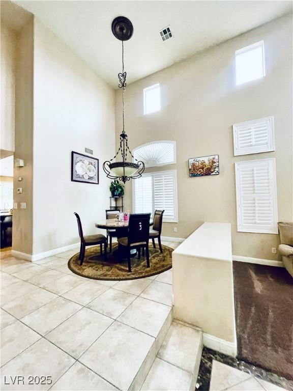 dining space featuring a towering ceiling, light tile patterned floors, baseboards, and visible vents