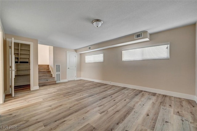 interior space featuring visible vents, stairway, light wood-style floors, a textured ceiling, and baseboards