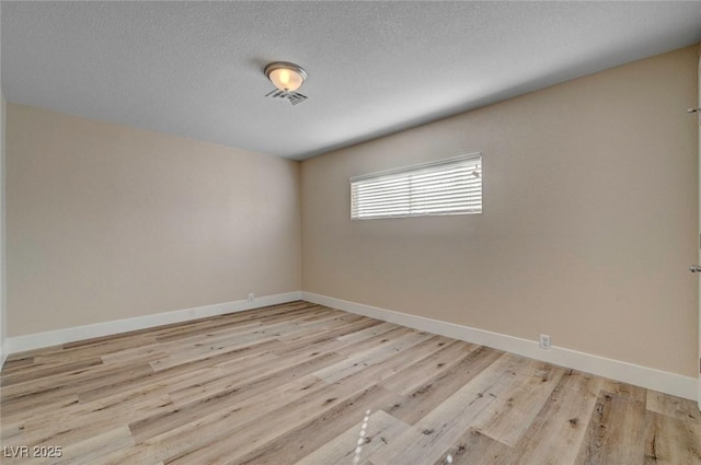 empty room featuring light wood-style floors, baseboards, and a textured ceiling