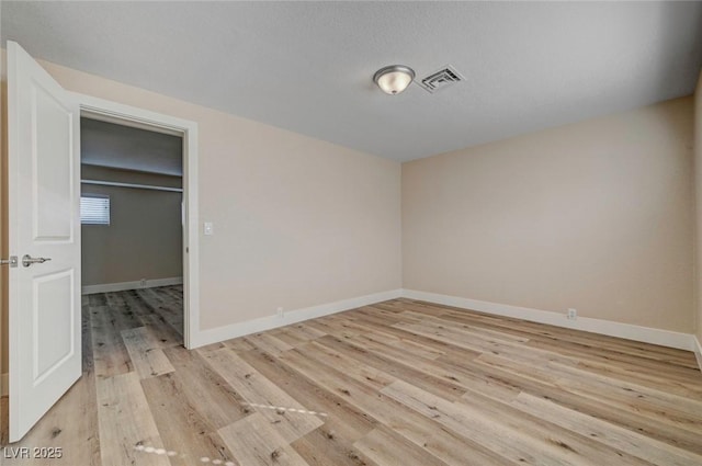 unfurnished bedroom with a spacious closet, light wood finished floors, visible vents, and baseboards