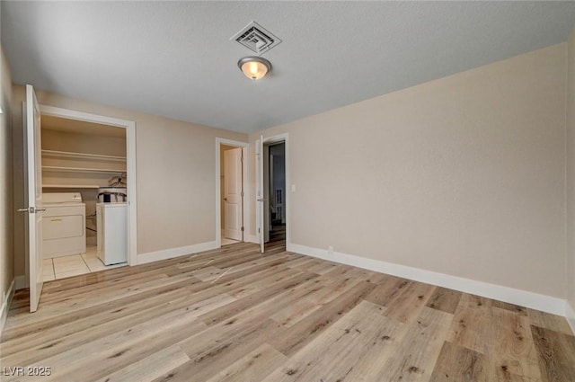 unfurnished bedroom with separate washer and dryer, light wood-type flooring, visible vents, and baseboards