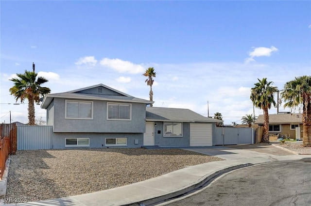 tri-level home with an attached garage, fence, driveway, a gate, and stucco siding