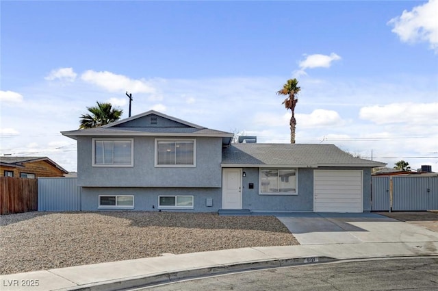 split level home with stucco siding, driveway, an attached garage, and fence