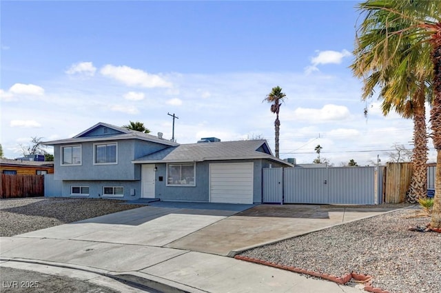 split level home featuring a gate, fence, concrete driveway, and stucco siding