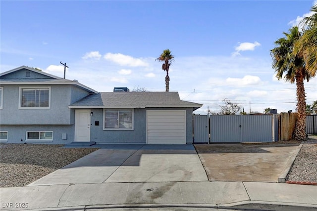 tri-level home with stucco siding, concrete driveway, a gate, fence, and a garage