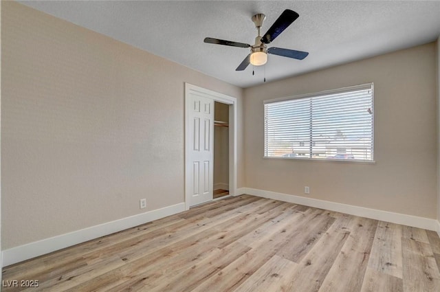 unfurnished bedroom featuring a textured ceiling, a closet, light wood-style flooring, and baseboards