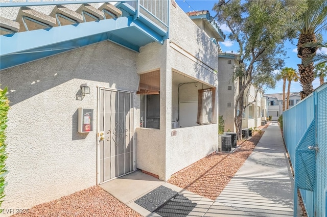 view of home's exterior featuring central AC unit, fence, a residential view, and stucco siding