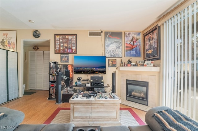 living room featuring a tile fireplace, visible vents, and wood finished floors