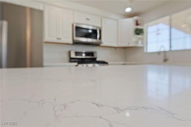 kitchen with open shelves, appliances with stainless steel finishes, white cabinetry, and light stone countertops