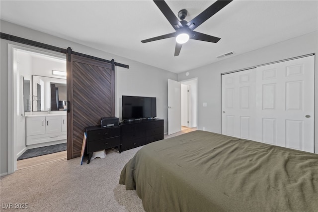 bedroom with a barn door, connected bathroom, carpet flooring, visible vents, and a closet