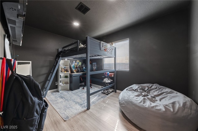 bedroom with a textured ceiling, wood finished floors, visible vents, and baseboards