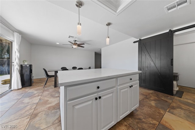 kitchen featuring a barn door, visible vents, white cabinets, hanging light fixtures, and light countertops