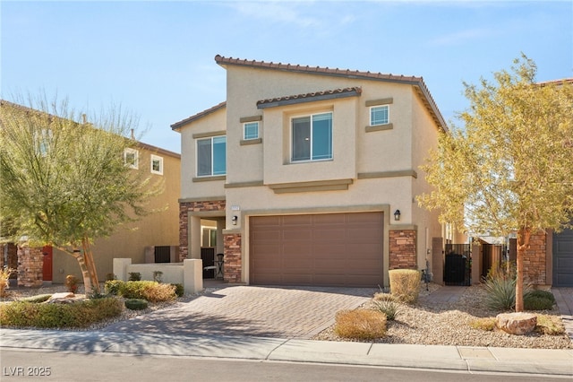 view of front of home with a garage, stone siding, decorative driveway, a gate, and stucco siding