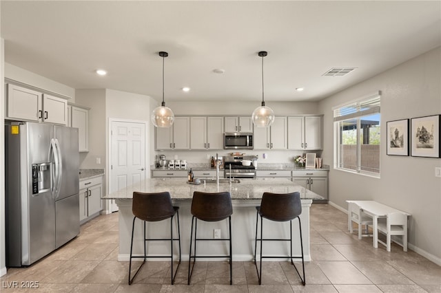 kitchen featuring stainless steel appliances, a breakfast bar, visible vents, and light stone countertops