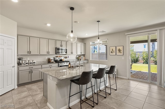 kitchen with a breakfast bar area, stainless steel appliances, gray cabinets, a healthy amount of sunlight, and a sink