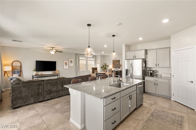 kitchen featuring light stone counters, visible vents, appliances with stainless steel finishes, open floor plan, and a sink