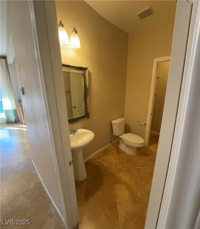 half bath with toilet, a sink, visible vents, and baseboards