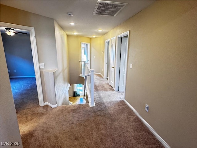 corridor featuring carpet, visible vents, baseboards, and an upstairs landing