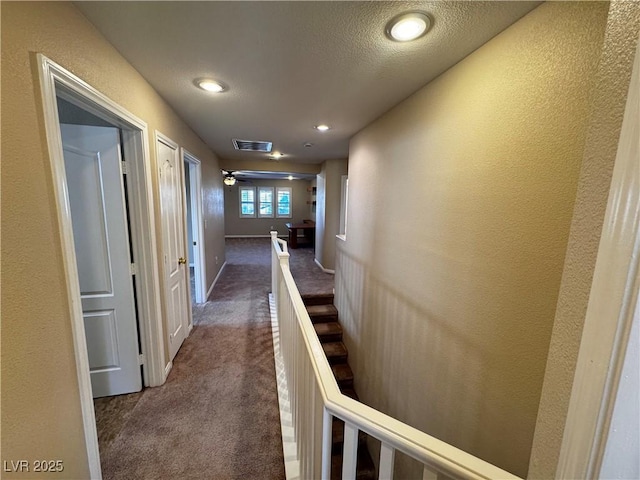 hallway with visible vents, a textured wall, dark carpet, a textured ceiling, and baseboards