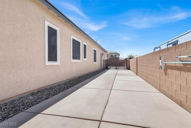 view of side of property with a gate, fence, and stucco siding