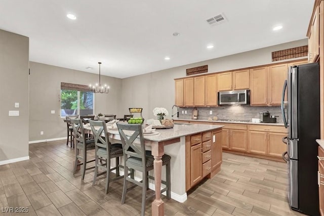 kitchen with a sink, visible vents, appliances with stainless steel finishes, tasteful backsplash, and a center island with sink