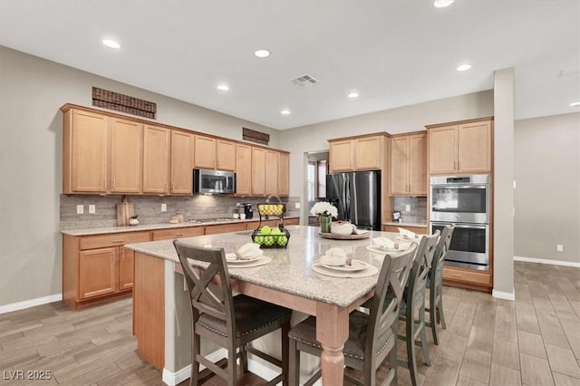 kitchen featuring decorative backsplash, a large island, a kitchen breakfast bar, light stone countertops, and stainless steel appliances