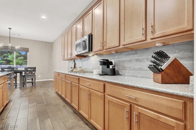 kitchen featuring stainless steel appliances, baseboards, light wood-style floors, hanging light fixtures, and decorative backsplash