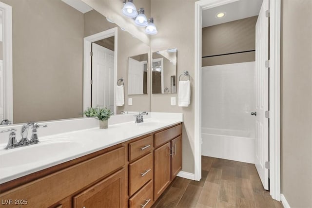 bathroom featuring double vanity, shower / washtub combination, a sink, and wood finished floors