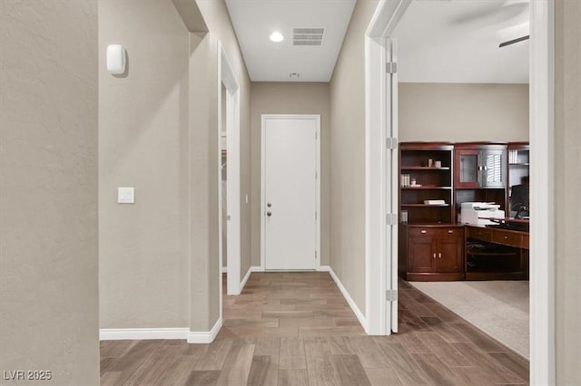 corridor featuring light wood finished floors, visible vents, and baseboards