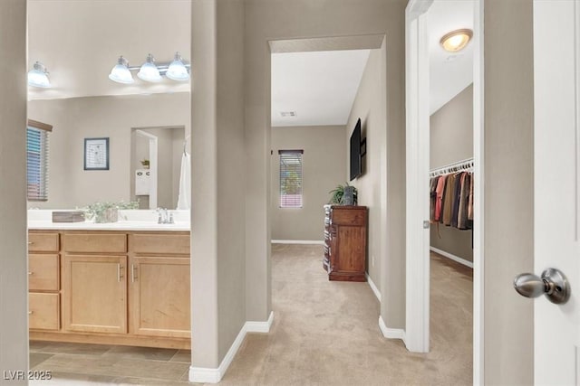 full bathroom featuring a walk in closet, vanity, and baseboards