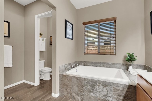 bathroom featuring toilet, vanity, wood finished floors, baseboards, and a bath