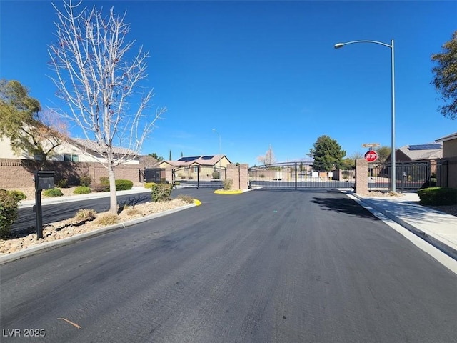 view of road featuring street lights, curbs, a gated entry, and a gate