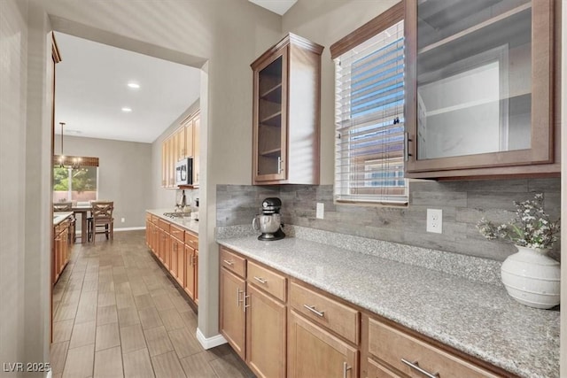 kitchen with glass insert cabinets, light countertops, stainless steel microwave, and decorative backsplash