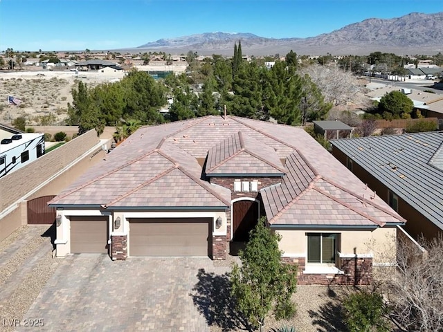 exterior space featuring an attached garage, a mountain view, stone siding, decorative driveway, and stucco siding