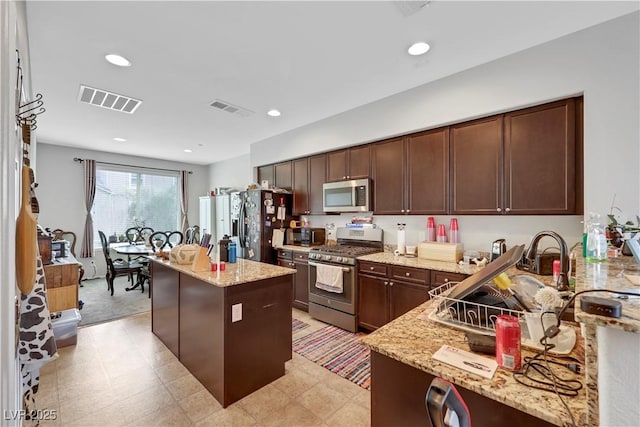 kitchen with a kitchen island, visible vents, stainless steel appliances, and light stone counters