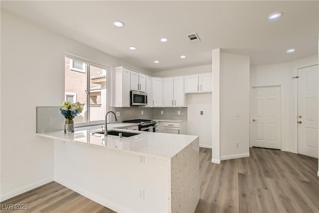 kitchen featuring light stone counters, light wood finished floors, appliances with stainless steel finishes, a sink, and a peninsula