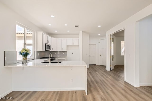 kitchen featuring decorative backsplash, stainless steel microwave, a peninsula, light wood-style floors, and white cabinetry