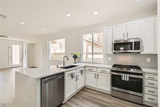 kitchen featuring stainless steel appliances, tasteful backsplash, light wood-style flooring, a sink, and a peninsula