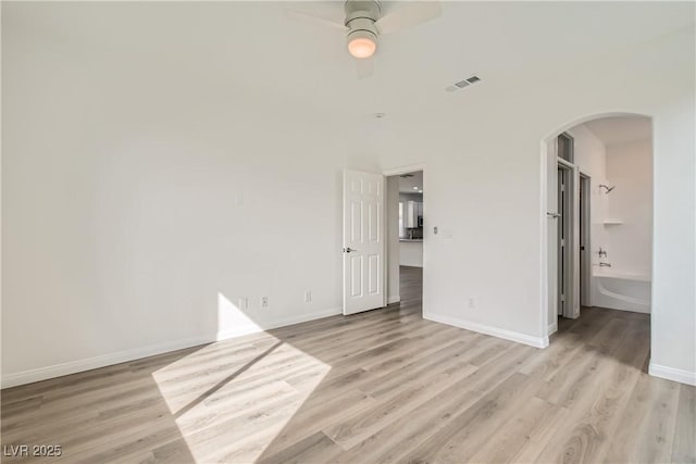 unfurnished bedroom featuring light wood-style floors, visible vents, arched walkways, and baseboards