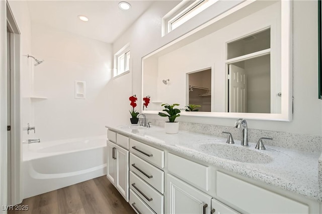 bathroom with a sink, a bathtub, wood finished floors, and double vanity