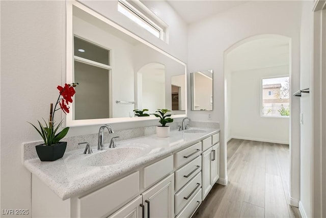 bathroom with double vanity, wood finished floors, a sink, and baseboards