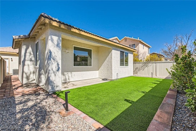 rear view of property with a lawn, a tile roof, fence, and stucco siding