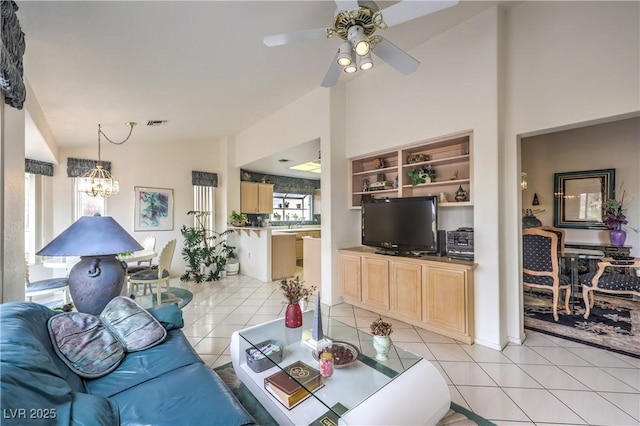 living area featuring lofted ceiling, light tile patterned flooring, visible vents, and ceiling fan with notable chandelier