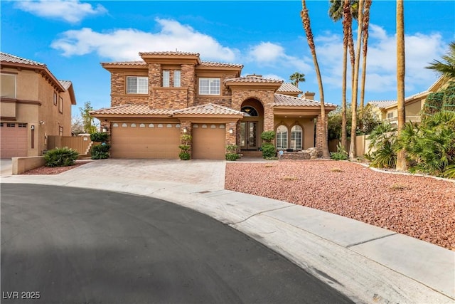 mediterranean / spanish house featuring stone siding, a tile roof, fence, and driveway