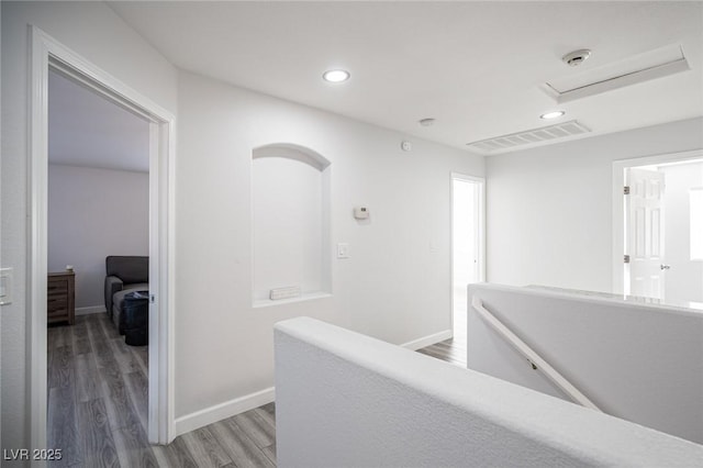 hallway with baseboards, visible vents, light wood-style flooring, and an upstairs landing