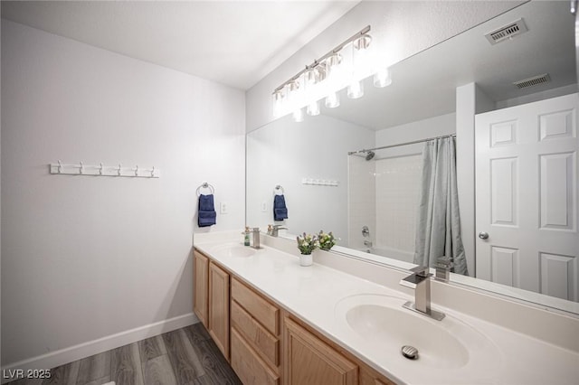 bathroom featuring wood finished floors, a sink, visible vents, baseboards, and double vanity