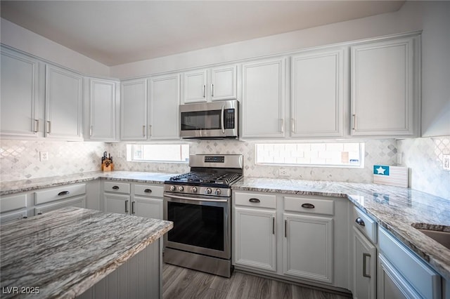 kitchen with appliances with stainless steel finishes, wood finished floors, backsplash, and light stone countertops