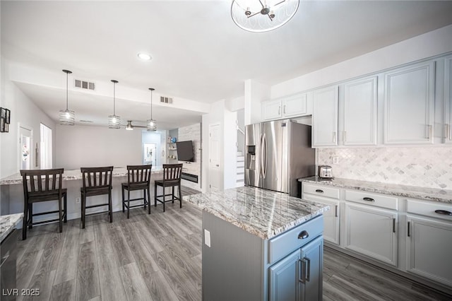 kitchen featuring stainless steel fridge, tasteful backsplash, visible vents, wood finished floors, and decorative light fixtures