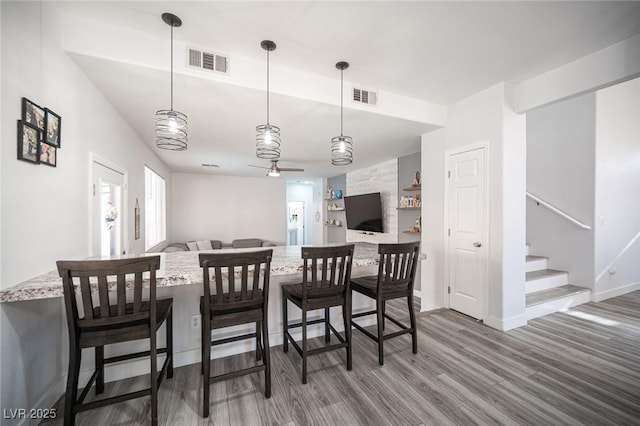 dining room featuring wood finished floors, visible vents, baseboards, and stairs